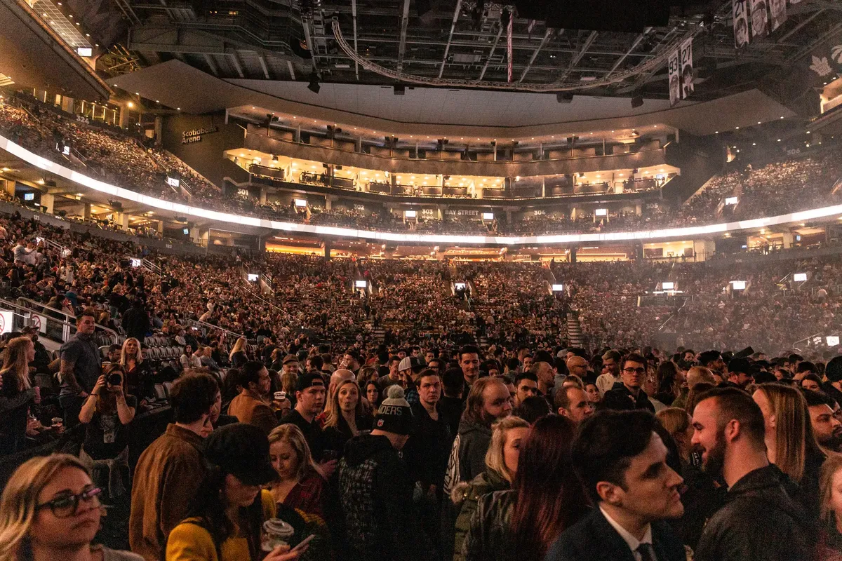 A large crowd gathers in an indoor arena for a lively event, surrounded by bright lights.