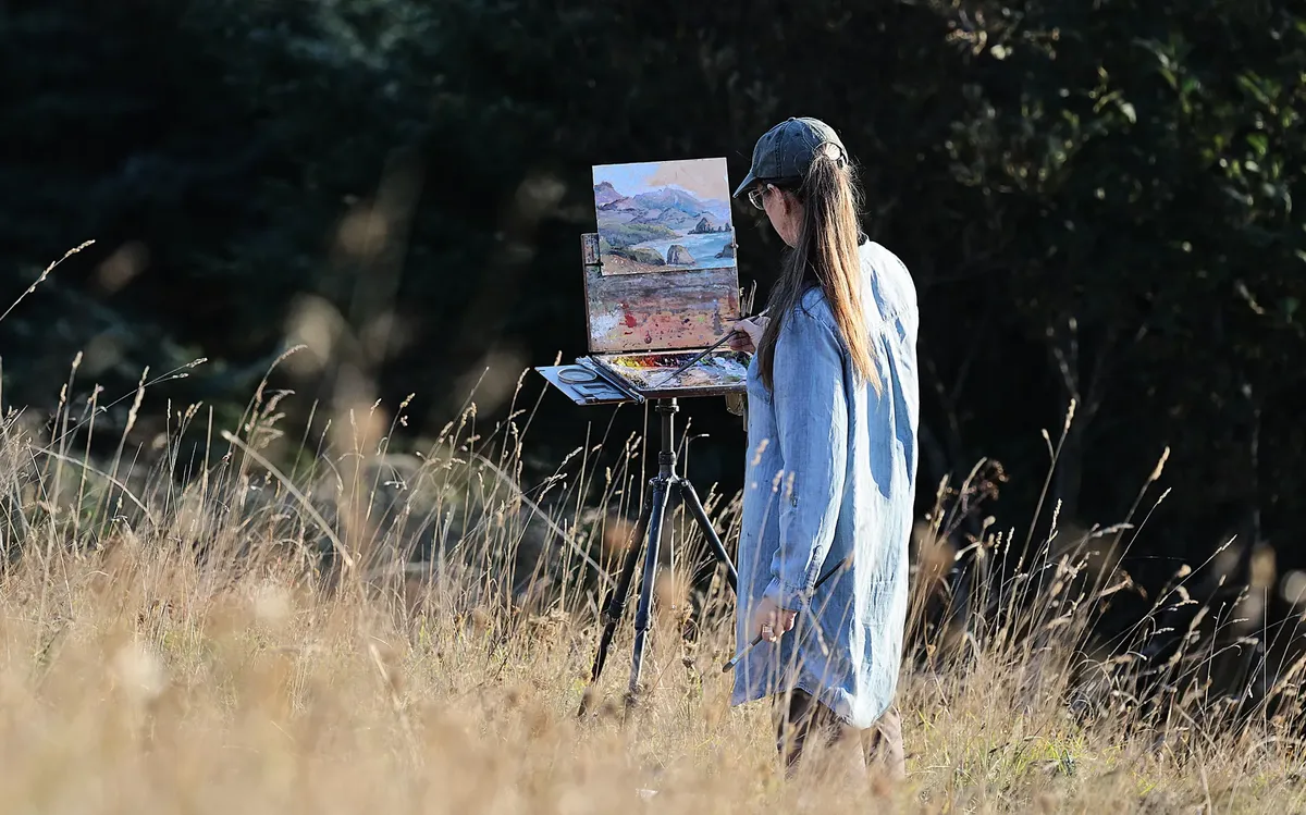 Woman painting landscape outdoors, showcasing the beauty of nature and art together.