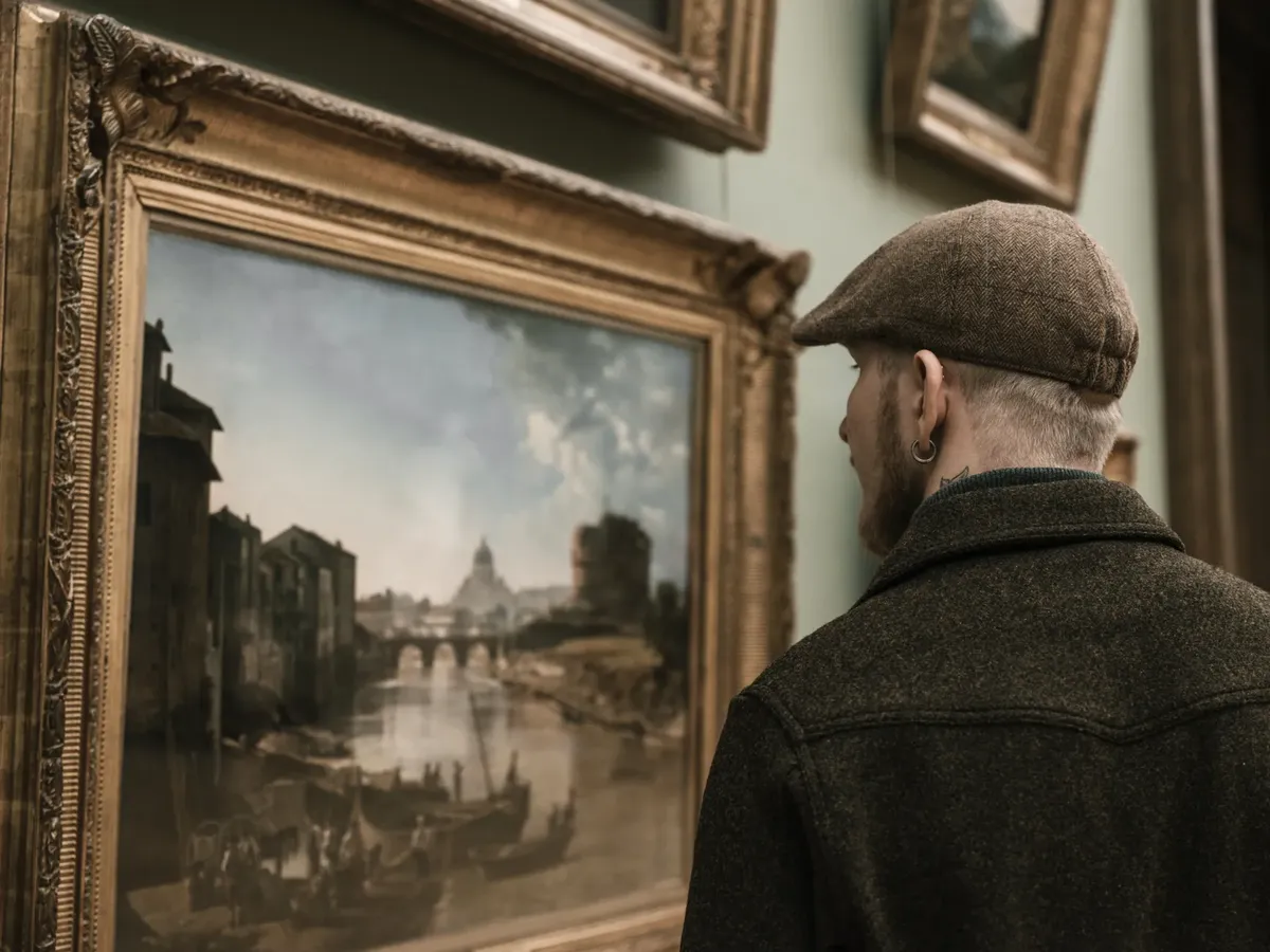 Man observing a classic landscape painting in a museum setting, showcasing art appreciation.