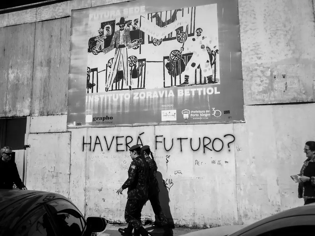 Black and white photo of an urban street scene with pedestrians and graffiti on a wall.