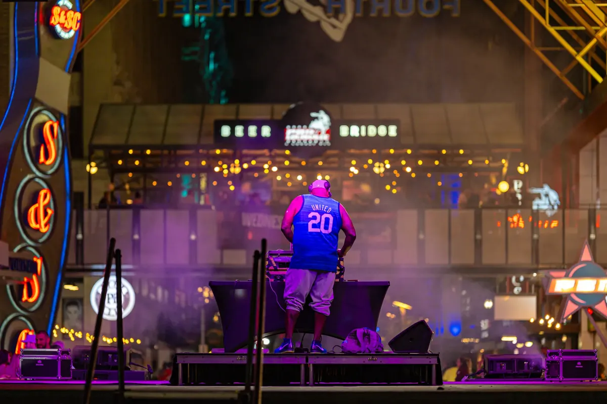 DJ performs amidst colorful lights at lively night street venue.