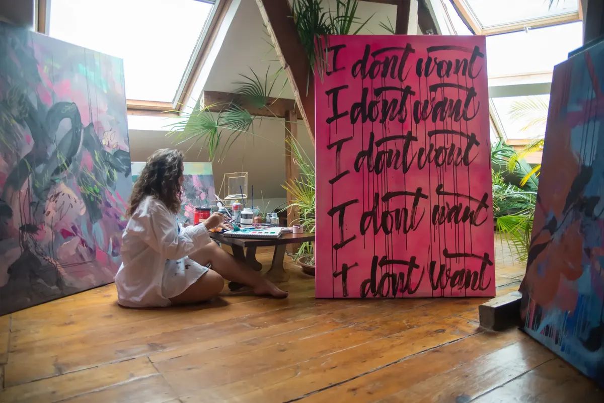 Woman artist painting abstract art in a well-lit studio loft with wooden floors.